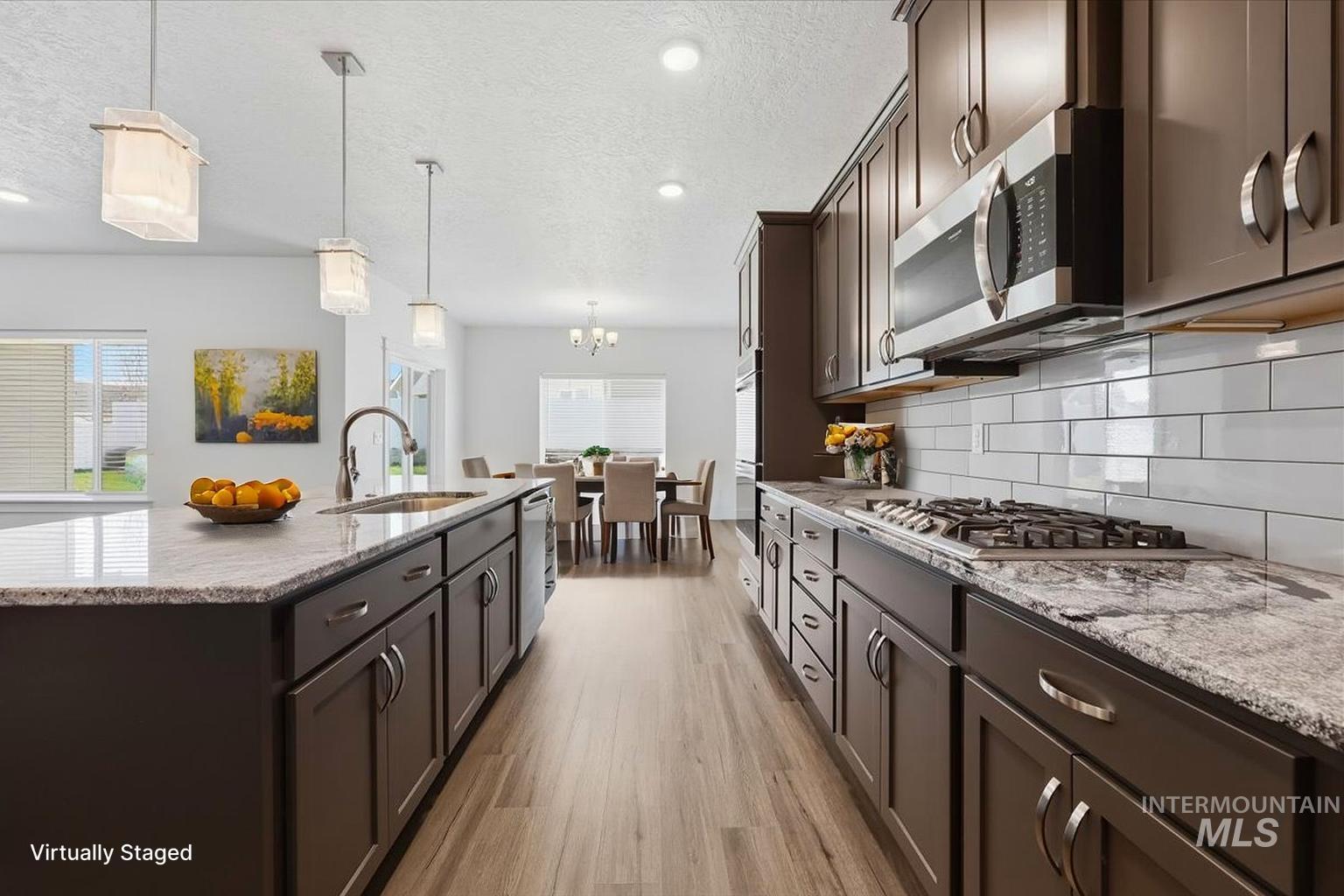 148 Homesteaders Street Middleton, ID 83644 - Photo 10 of 45 Kitchen featuring dark wood finish cabinets, light stone counters, stainless steel appliances, and a textured ceiling