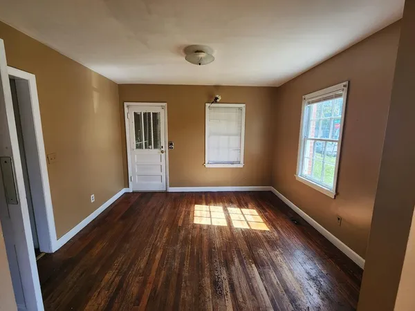 a view of an empty room with wooden floor and a window