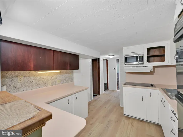 a living room with stainless steel appliances kitchen island granite countertop a refrigerator a stove a microwave oven with white cabinets and wooden floor