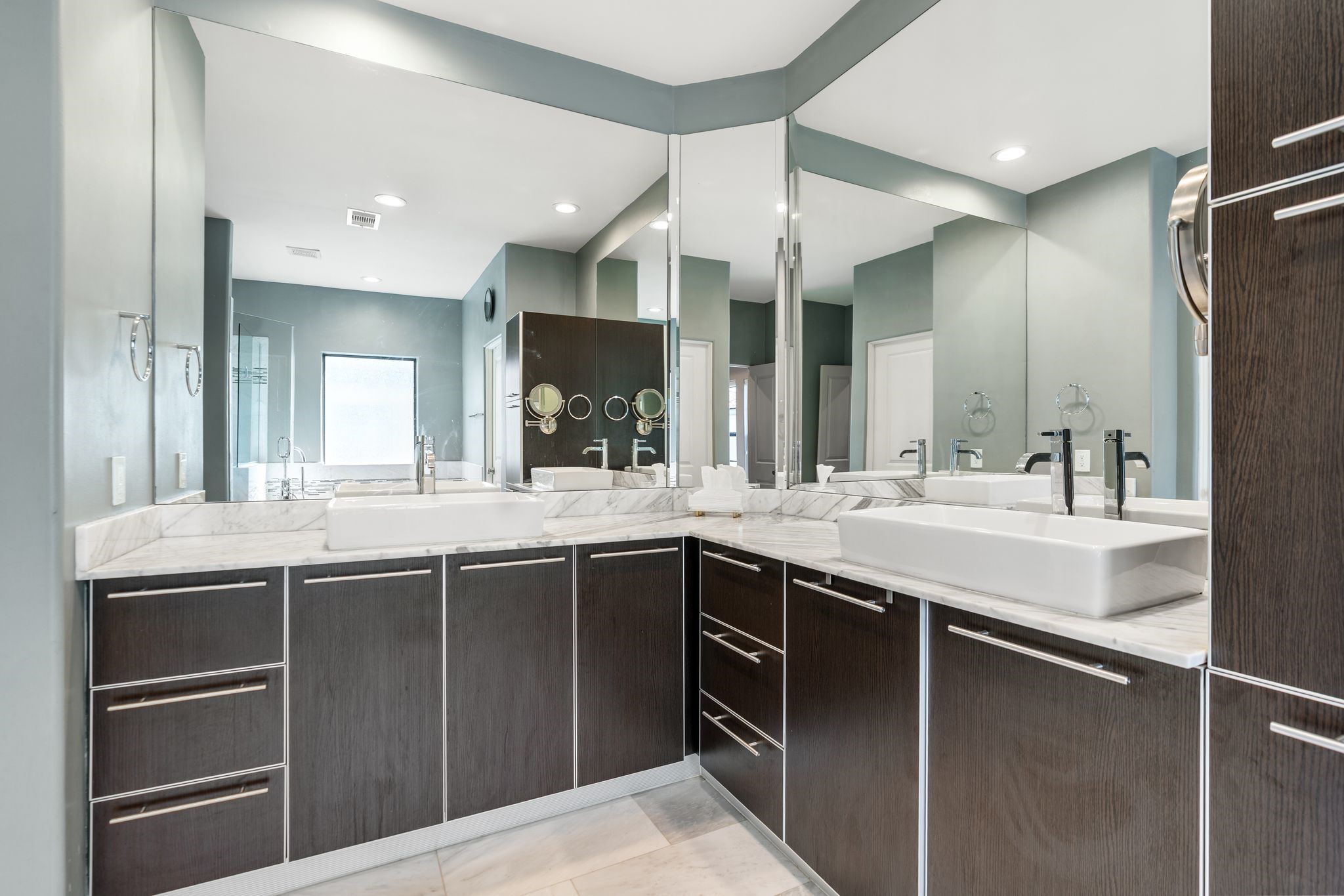 3934 Feagan Street Houston, TX 77007 - Photo 15 of 27 The ensuite primary bath has two large vanities with dual vessel sinks and a wide marble countertop. Modern wood cabinetry with chrome hardware provides ample drawer and cabinet storage. An oversized mirror spans the wall, making the space feel open and functional.