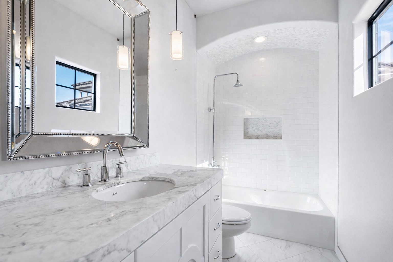 3934 Feagan Street Houston, TX 77007 - Photo 19 of 27 The secondary bathroom features a marble vanity, framed mirror, and two modern pendant lights. The tub/ shower features updated subway tile with a built-in soap niche and a barrel tile ceiling detail overhead. A window adds natural light while maintaining a clean, bright look.