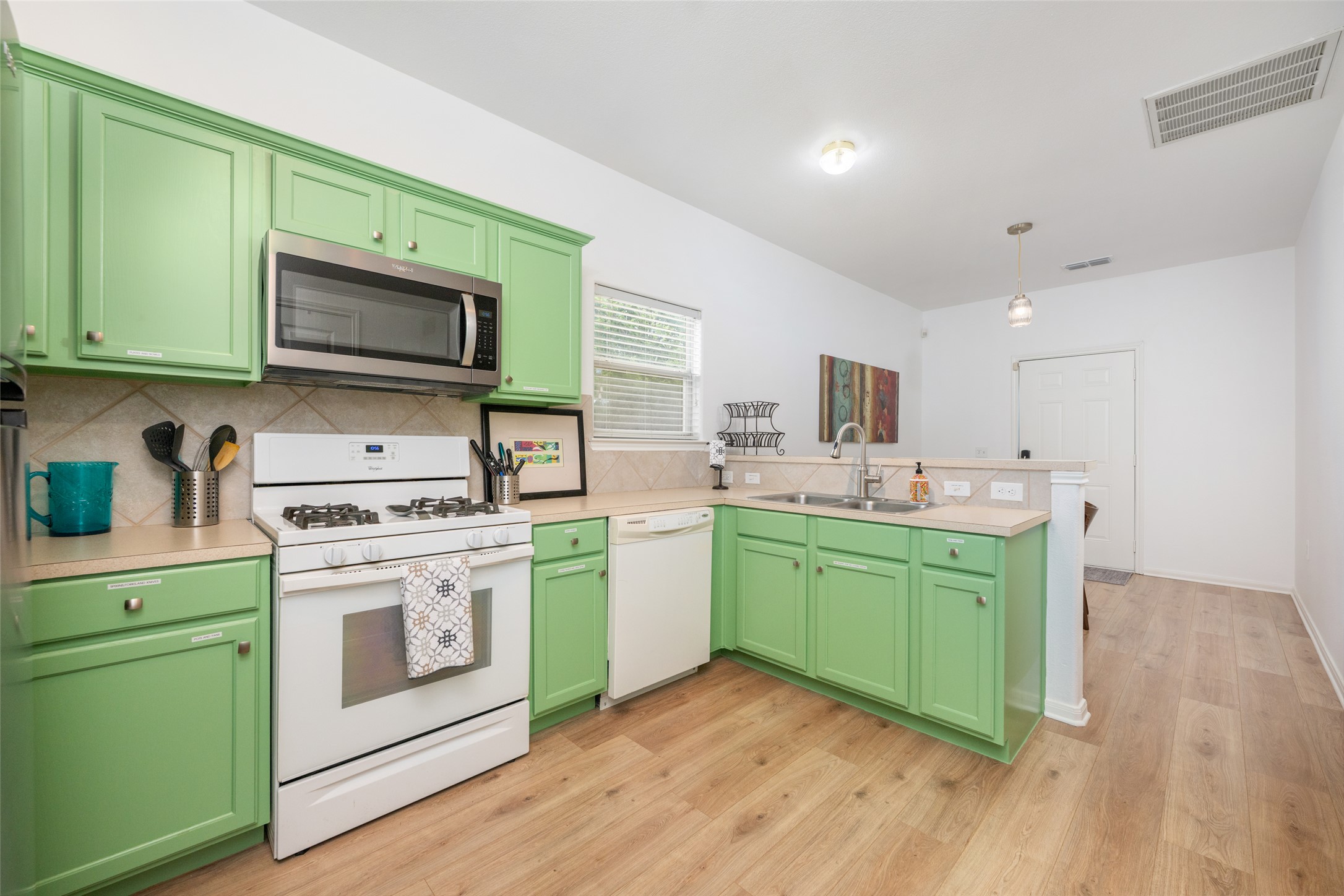 5613 Signal Point Austin, TX 78724 - Photo 10 of 21 Kitchen featuring wood-finish flooring, light green cabinetry, white appliances, stainless steel microwave, and a double basin sink