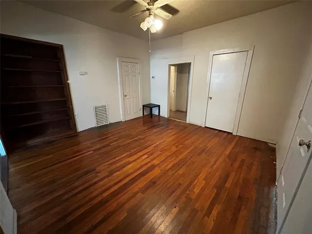 a view of an empty room with wooden floor and a ceiling fan