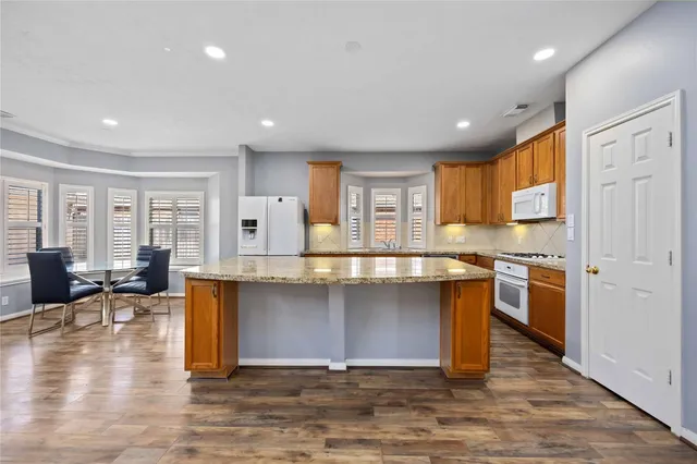 a kitchen with stainless steel appliances granite countertop a stove top oven a sink dishwasher a dining table and chairs with wooden floor