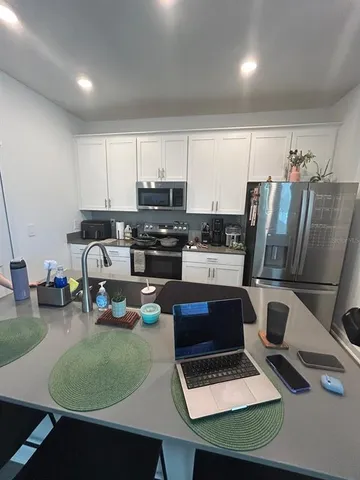 a living room with stainless steel appliances furniture a rug and a kitchen view