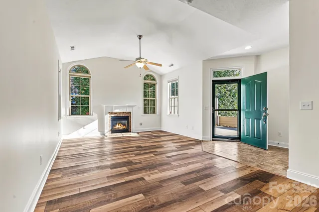 a view of an empty room with wooden floor fireplace and a window