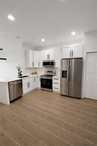 a large kitchen with granite countertop a stove top oven a sink and dishwasher a refrigerator with white cabinets