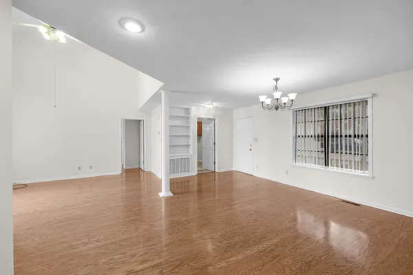 an empty room with chandelier fan and windows