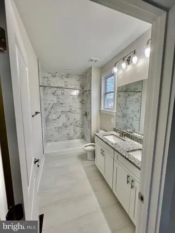 a bathroom with a granite countertop sink a toilet a mirror and shower