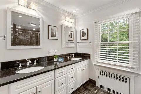 a bathroom with a granite countertop double vanity sink a two mirror a window and a bathtub