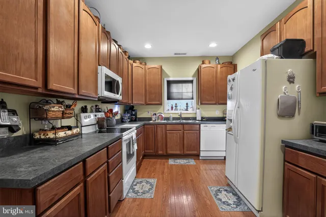 a kitchen with stainless steel appliances granite countertop a refrigerator a stove and a sink with wooden floors