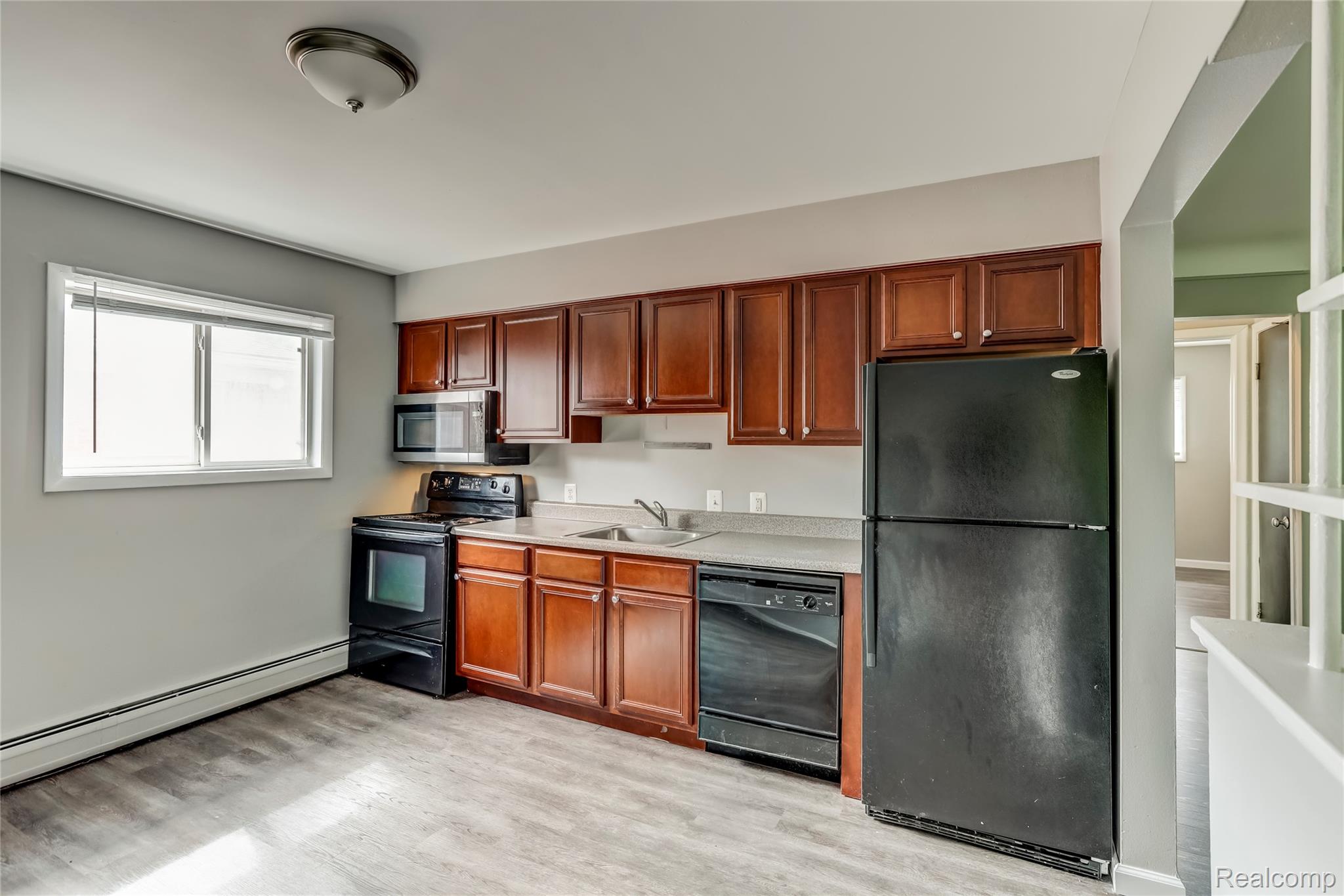 649 West Maple Road, Unit 8 Clawson, MI 48017 - Photo 2 of 16 Kitchen featuring wood-finish flooring, dark wood cabinetry, black appliances, light-toned countertops, and a window for natural illumination