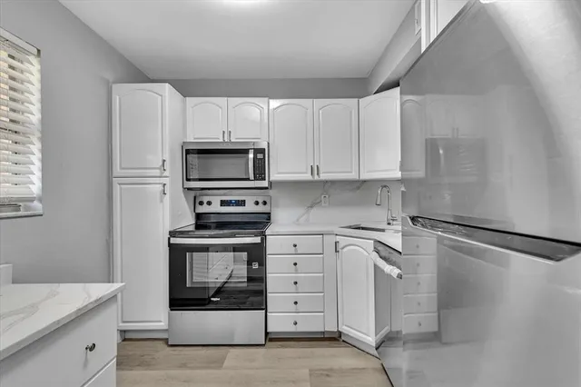 a kitchen with granite countertop white cabinets stainless steel appliances and a window