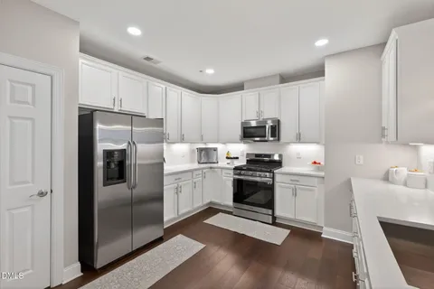 a kitchen with granite countertop a stove a sink dishwasher and white cabinets with wooden floor