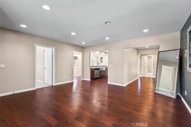a view of an empty room with wooden floor kitchen view and a window