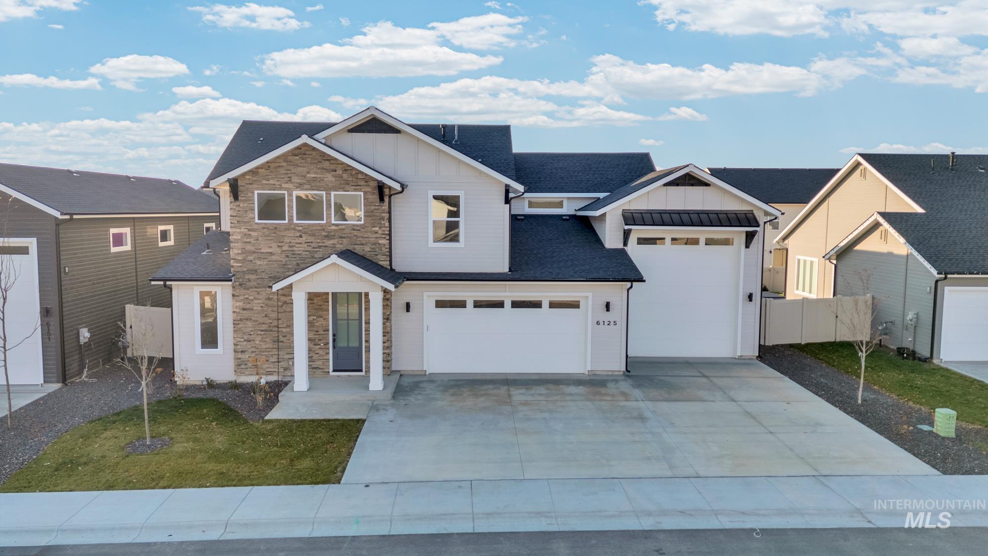 View of front facade with board and batten siding, stone siding, concrete driveway, and roof with shingles