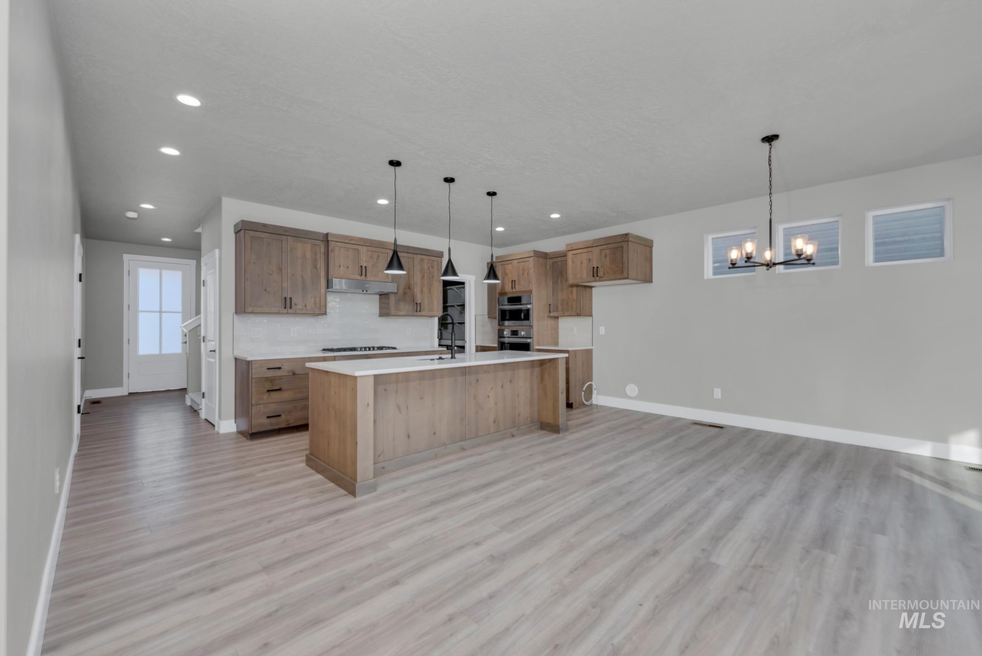 2807 West Jutland Street Meridian, ID 83642 - Photo 4 of 25 Kitchen with brown cabinets, decorative light fixtures, a center island with sink, light wood-style floors, and recessed lighting