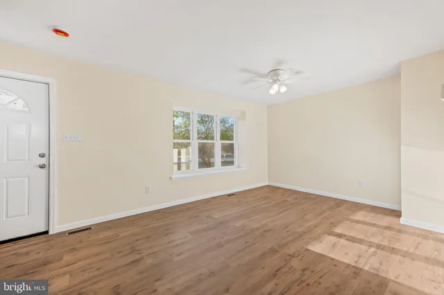 an empty room with wooden floor ceiling fan and windows