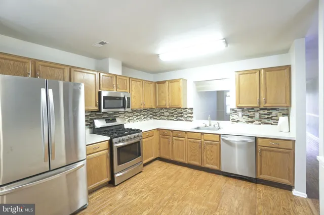 a kitchen with stainless steel appliances granite countertop a stove top oven a refrigerator a sink and dishwasher with wooden floor