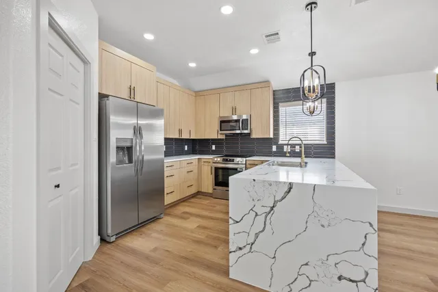 a kitchen with stainless steel appliances granite countertop a refrigerator a sink dishwasher a stove and white cabinets with wooden floor