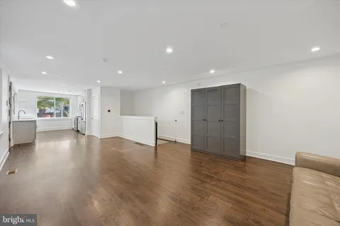 a view of an empty room with wooden floor and a kitchen