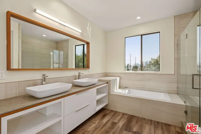 a bathroom with a two sinks a large mirror and a bathtub next to a window