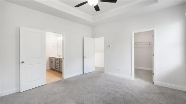 an empty room with chandelier fan and kitchen view