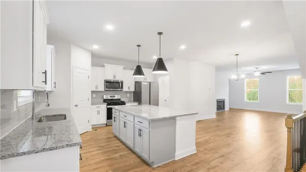 a large kitchen with stainless steel appliances kitchen island granite countertop a stove a sink a refrigerator and white cabinets with wooden floor