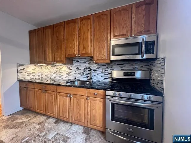a kitchen with granite countertop wood cabinets stainless steel appliances and a sink
