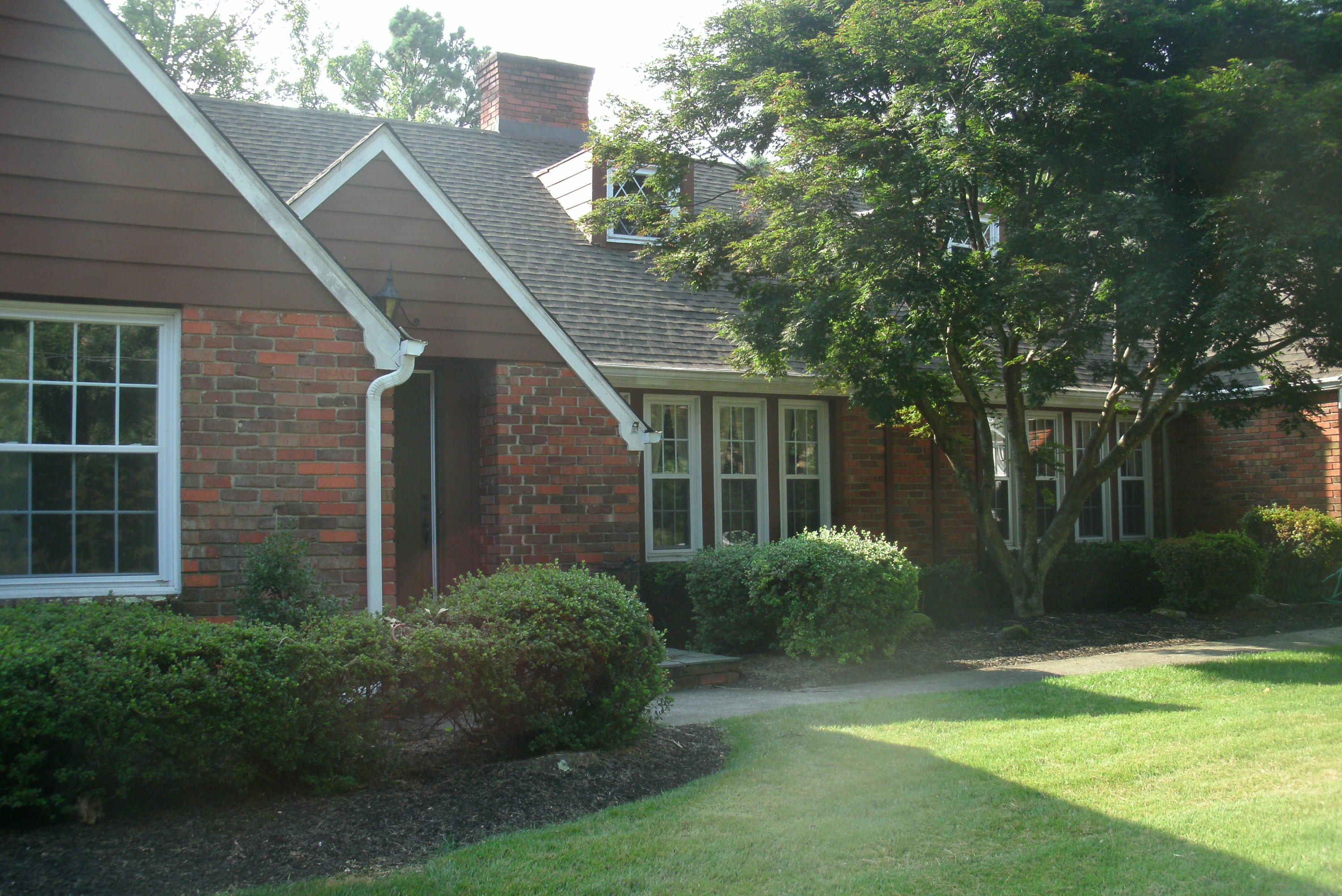 a view of a house with brick walls plants and large tree