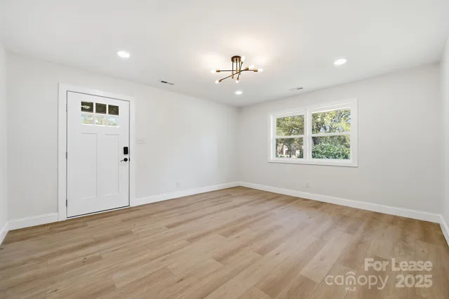 an empty room with wooden floor chandelier and windows