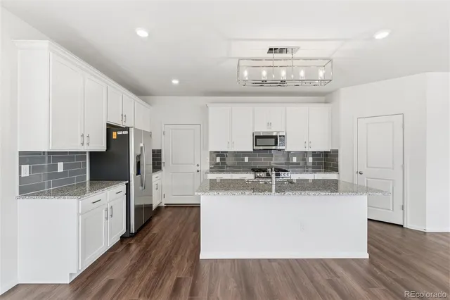 a kitchen with stainless steel appliances a stove a refrigerator and white cabinets with wooden floor