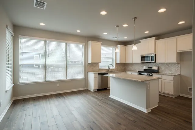 a large kitchen with stainless steel appliances granite countertop a stove a sink dishwasher a refrigerator and white cabinets with wooden floor