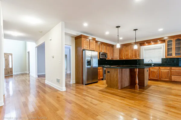 a kitchen with stainless steel appliances granite countertop a refrigerator a sink dishwasher a stove and a dining table with wooden floor
