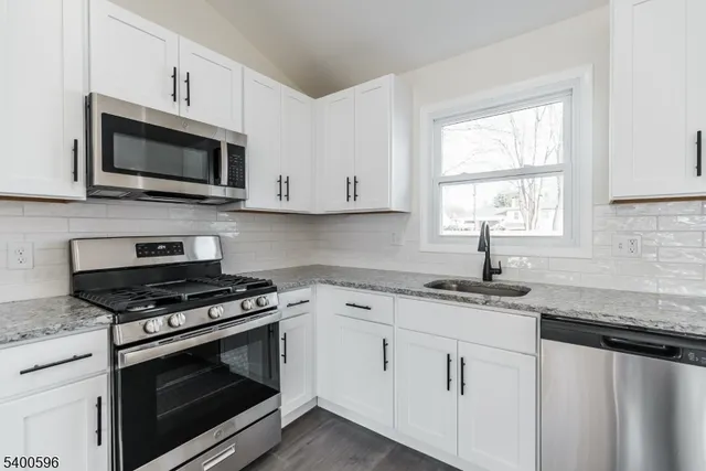 a kitchen with granite countertop white cabinets appliances a window and a sink