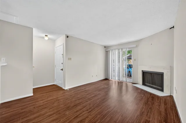 a view of an empty room with wooden floor fireplace and a window