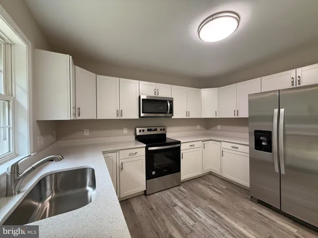 a kitchen with granite countertop white cabinets appliances a window and a sink