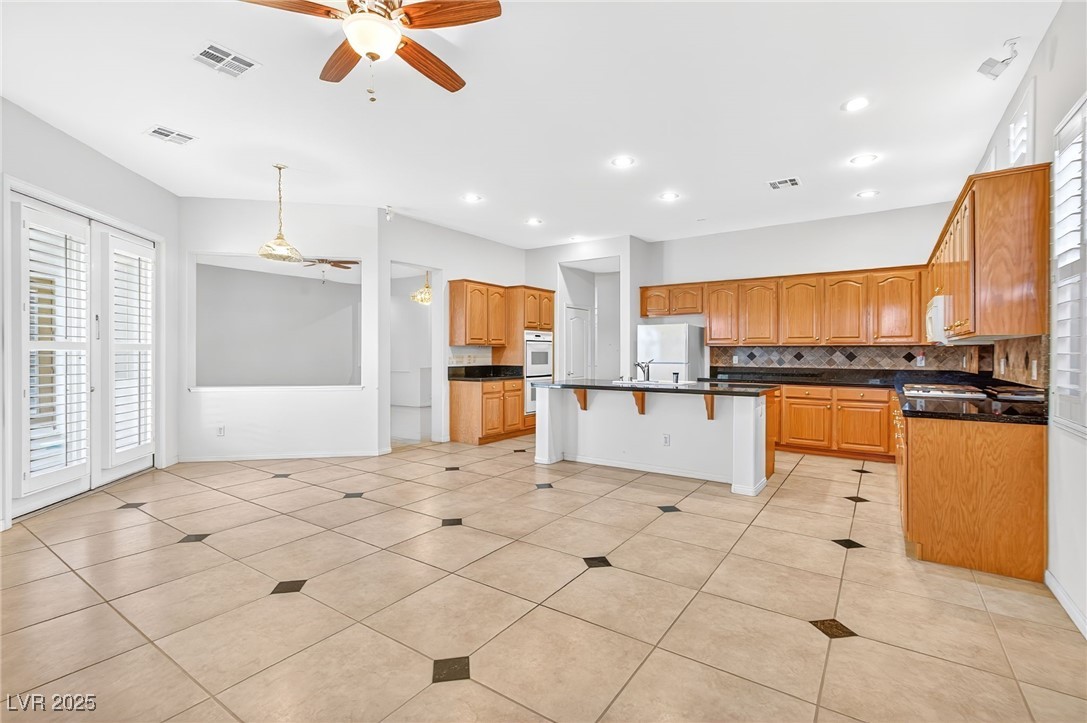 1028 Triumphant Street Henderson, NV 89052 - Photo 12 of 51 Kitchen featuring a breakfast bar area, light tile patterned floors, white appliances, tasteful backsplash, and a ceiling fan