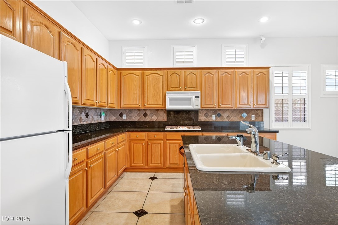 1028 Triumphant Street Henderson, NV 89052 - Photo 15 of 51 Kitchen featuring white appliances, light tile patterned floors, Granite Countertops, tasteful backsplash, and recessed lighting