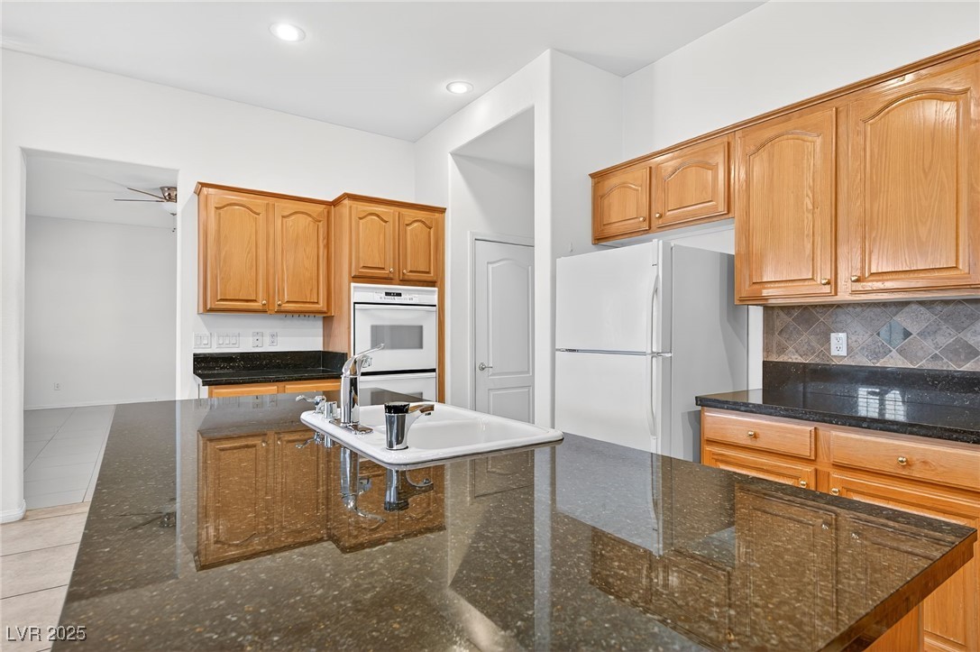 1028 Triumphant Street Henderson, NV 89052 - Photo 16 of 51 Kitchen featuring white appliances, Granite Countertops, brown cabinets, tasteful backsplash, and light tile patterned flooring