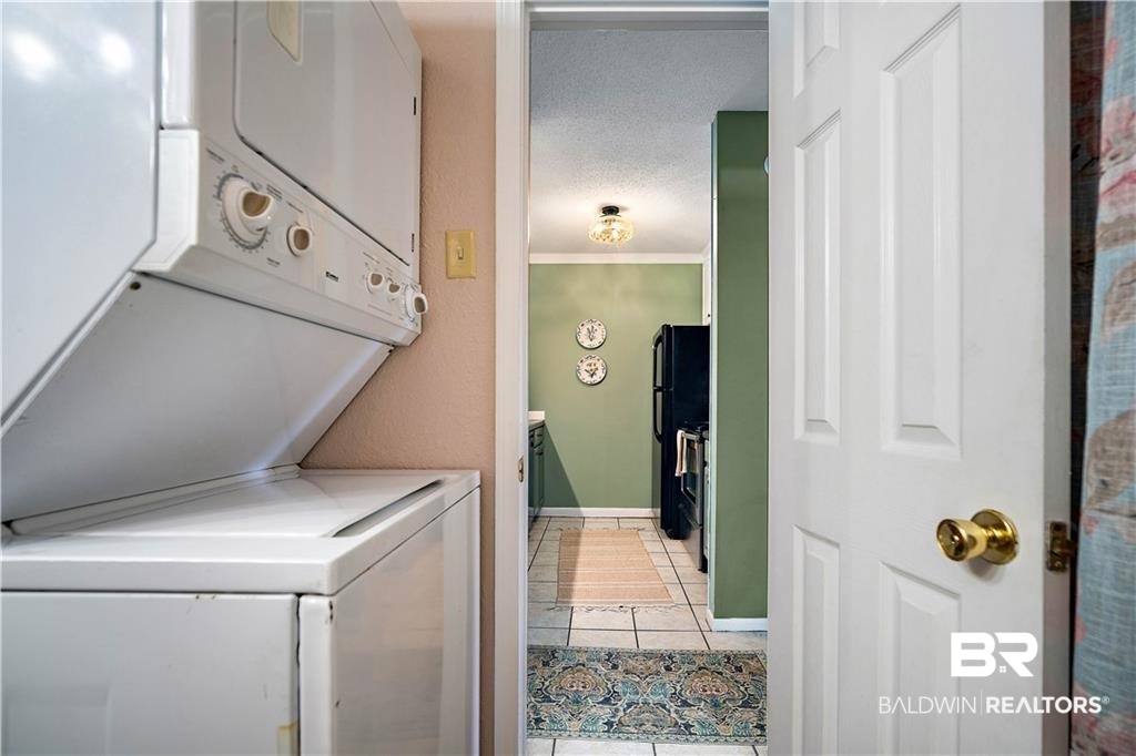 239 Riverbend Drive, Unit 239 Mobile, AL 36605 - Photo 26 of 26 Laundry area with crown molding, stacked washing maching and dryer, and tile patterned flooring