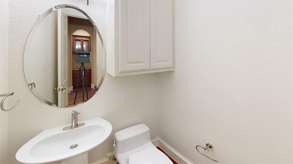 4516 Gilbert Avenue Dallas, TX 75219 - Photo 18 of 28 Pedestal sink with a polished chrome faucet, oval beveled mirror, and white wall-mounted cabinetry