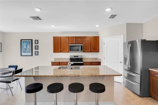 a kitchen with stainless steel appliances granite countertop a refrigerator a stove a sink counter tops and chairs with wooden floor