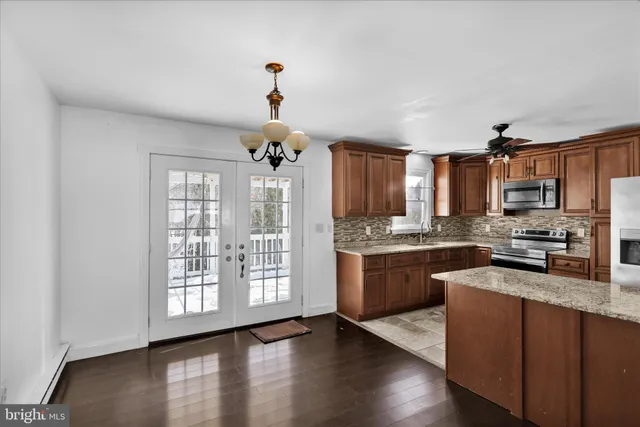 a kitchen with stainless steel appliances granite countertop a stove top oven a sink dishwasher a refrigerator and a dining table with wooden floor