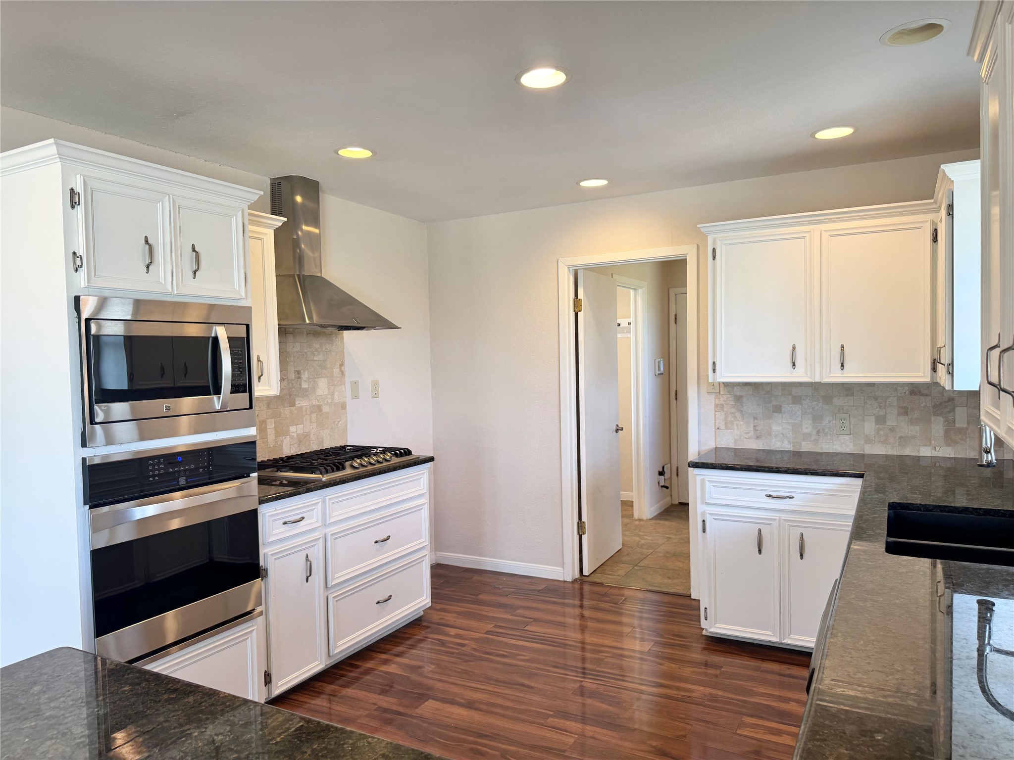 18512 Carlson Lane Elgin, TX 78621 - Photo 7 of 29 Rich hardwood flooring complements custom white cabinetry and polished granite countertops in this modern kitchen.