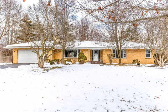 a front view of a house with a yard covered with snow and trees