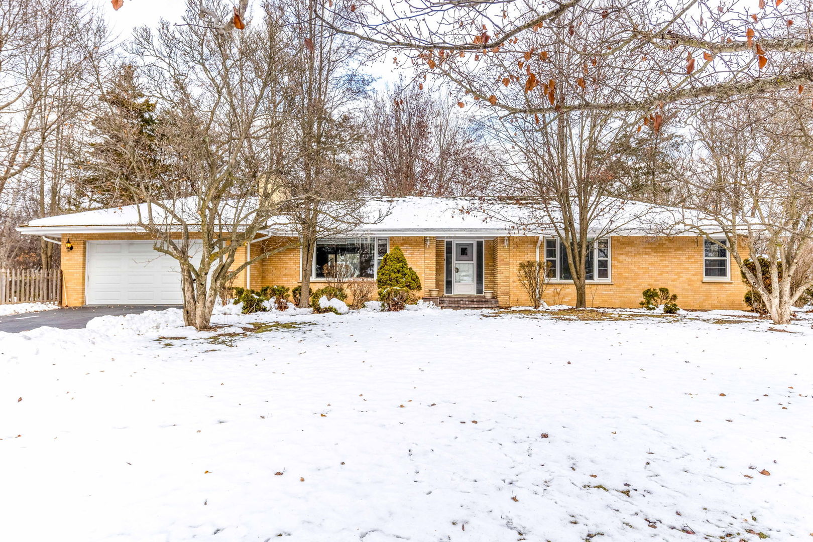 a front view of a house with a yard covered with snow and trees