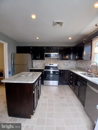 a kitchen with kitchen island granite countertop a sink a counter top space and stainless steel appliances