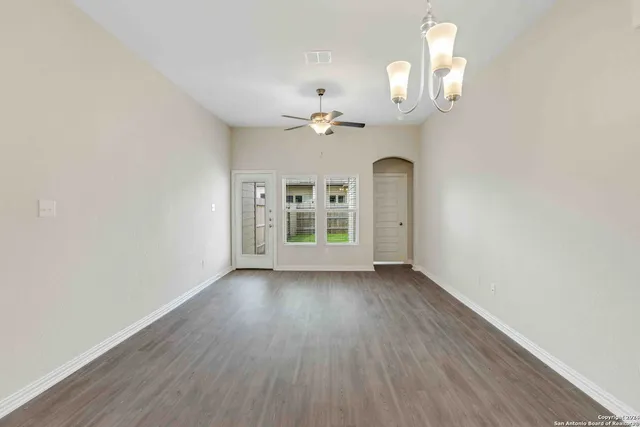 an empty room with wooden floor chandelier fan and windows