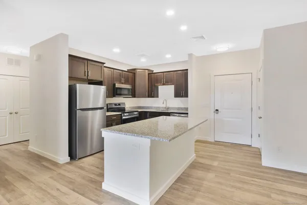 a large kitchen with a refrigerator a sink dishwasher a oven with white cabinets and wooden floor